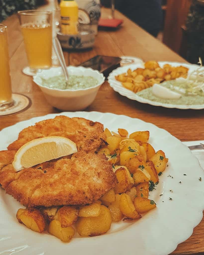 Delicious crispy schnitzel with golden potatoes and refreshing drinks on a wooden table.