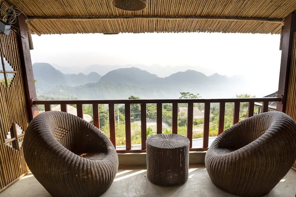Comfortable armchairs and small side table on veranda near wooden barrier overlooking mountain ridge and green trees in tropical country