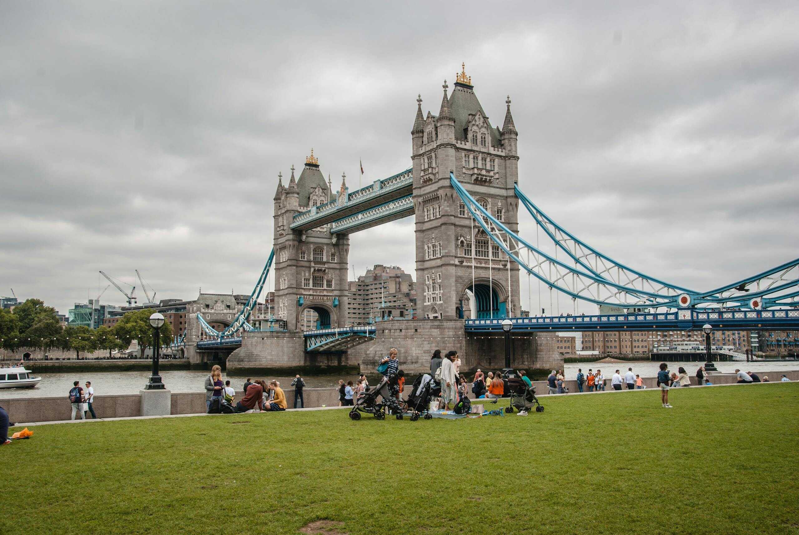 Iconic Tower Bridge in London with people enjoying a park view on a cloudy day.